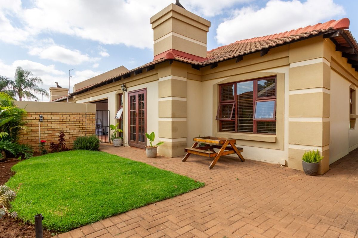 A well-maintained rear exterior view of the townhouse featuring a brick-paved patio, a small garden area, and classic architectural details including a chimney stack.