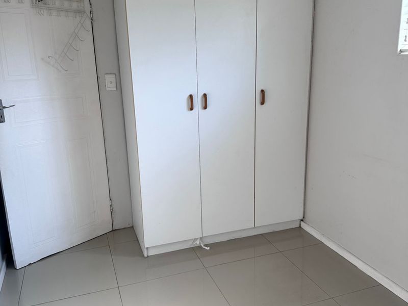 A clean, empty bedroom featuring neutral tiled flooring and a functional built-in wardrobe with white cabinetry.