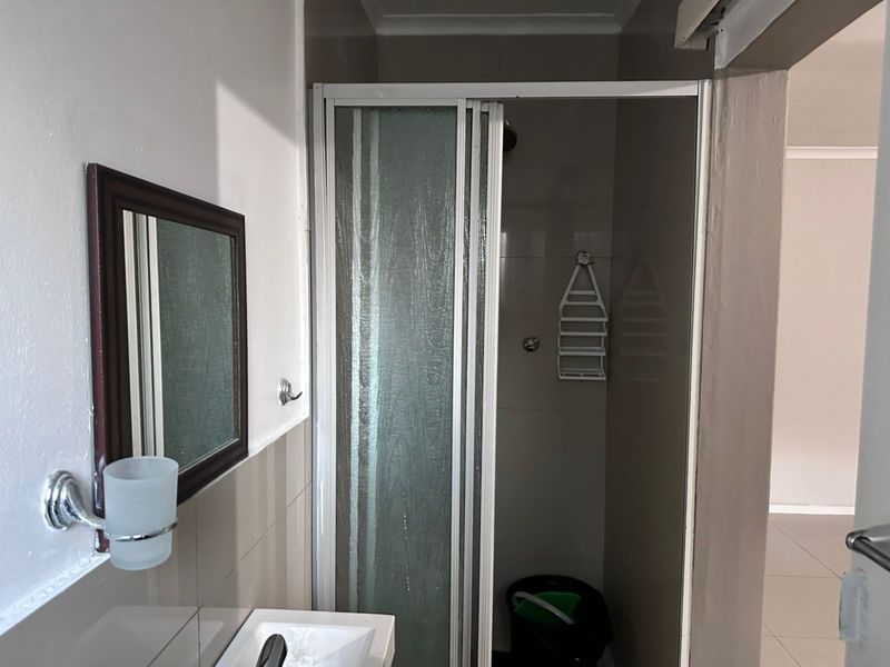 A functional bathroom featuring a shower enclosure with sliding doors, a wall-mounted basin, and neutral wall tiling.