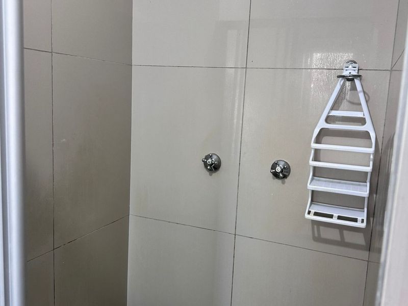 A functional shower enclosure featuring neutral wall tiling, a standard shower head, and dual mixer taps.