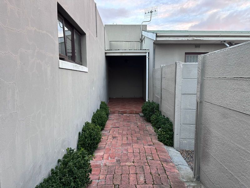 A narrow exterior side passage featuring brick paving, a covered walkway area, and boundary walling with visible plaster cracking.