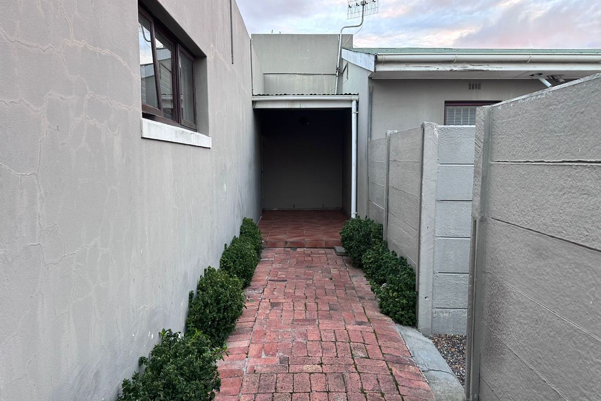 A narrow exterior side passage featuring brick paving, a covered walkway area, and boundary walling with visible plaster cracking.