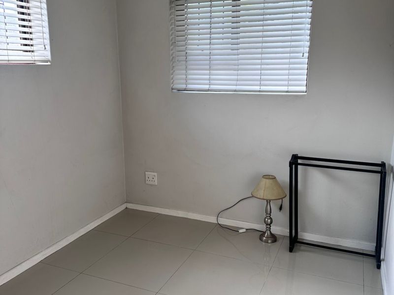 A bright, empty bedroom featuring neutral tiled flooring, clean walls, and fitted venetian blinds, offering a versatile space ready for personalization.