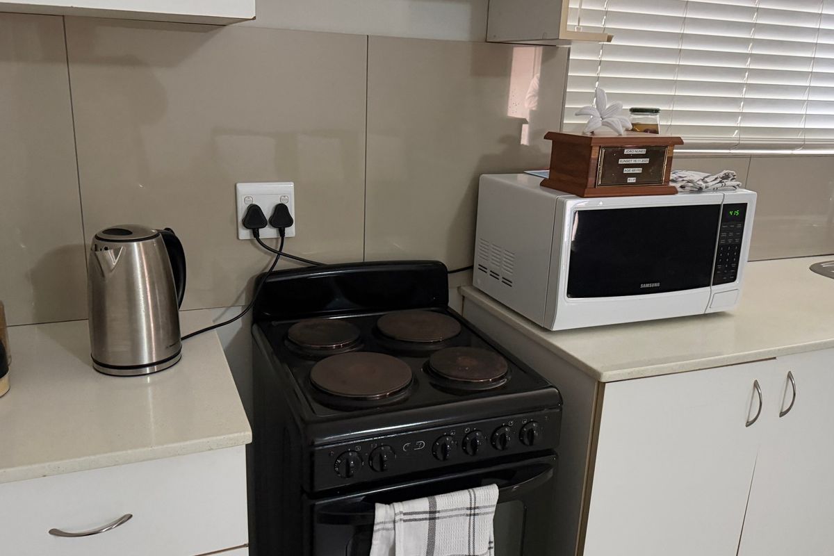 A functional kitchen area featuring built-in cabinetry, a solid surface countertop, a tiled splashback, and a freestanding electric stove.