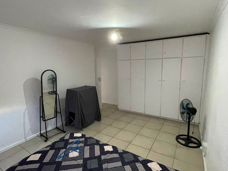 A bedroom featuring neutral tiled flooring and a wall of white built-in cupboards providing ample storage space.