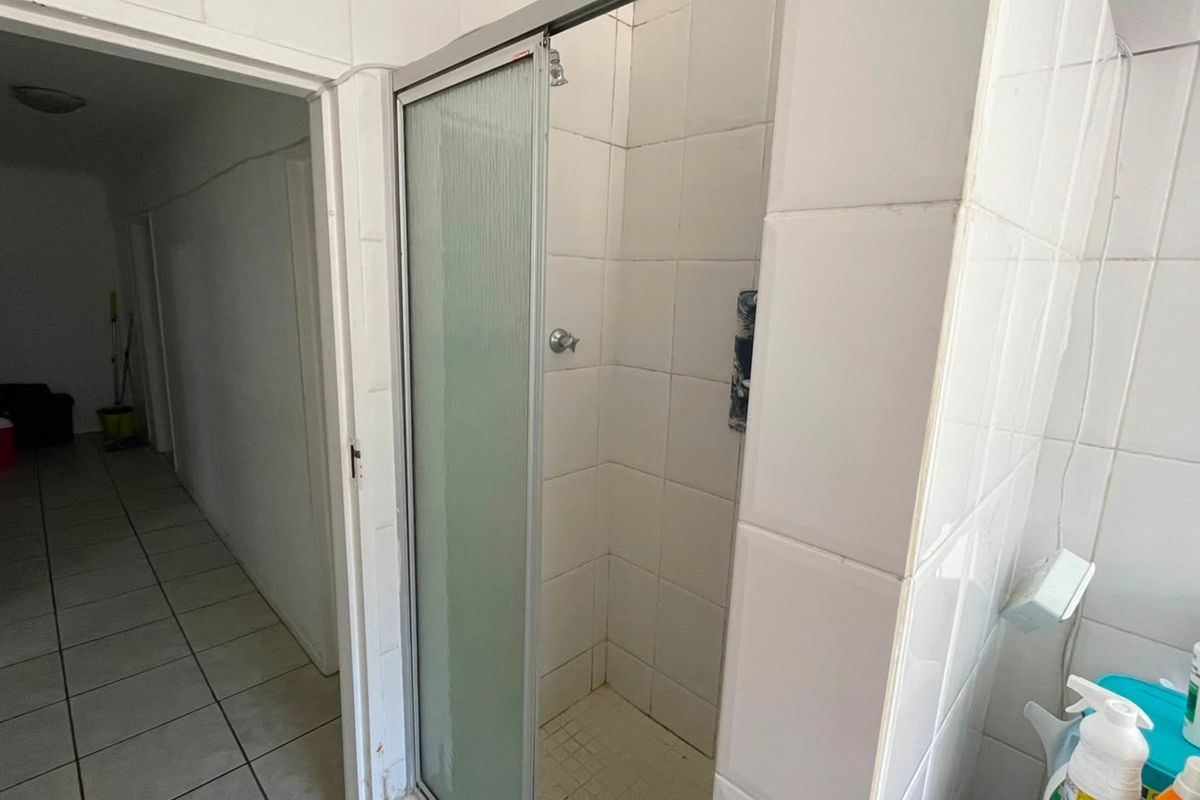 A functional bathroom featuring a tiled shower enclosure with a glass door, requiring some cosmetic updates to the finishes.