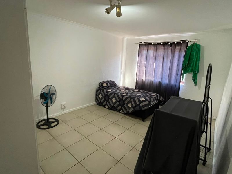 A simple bedroom featuring tiled flooring, a central ceiling light fixture, and a window with a curtain rod.