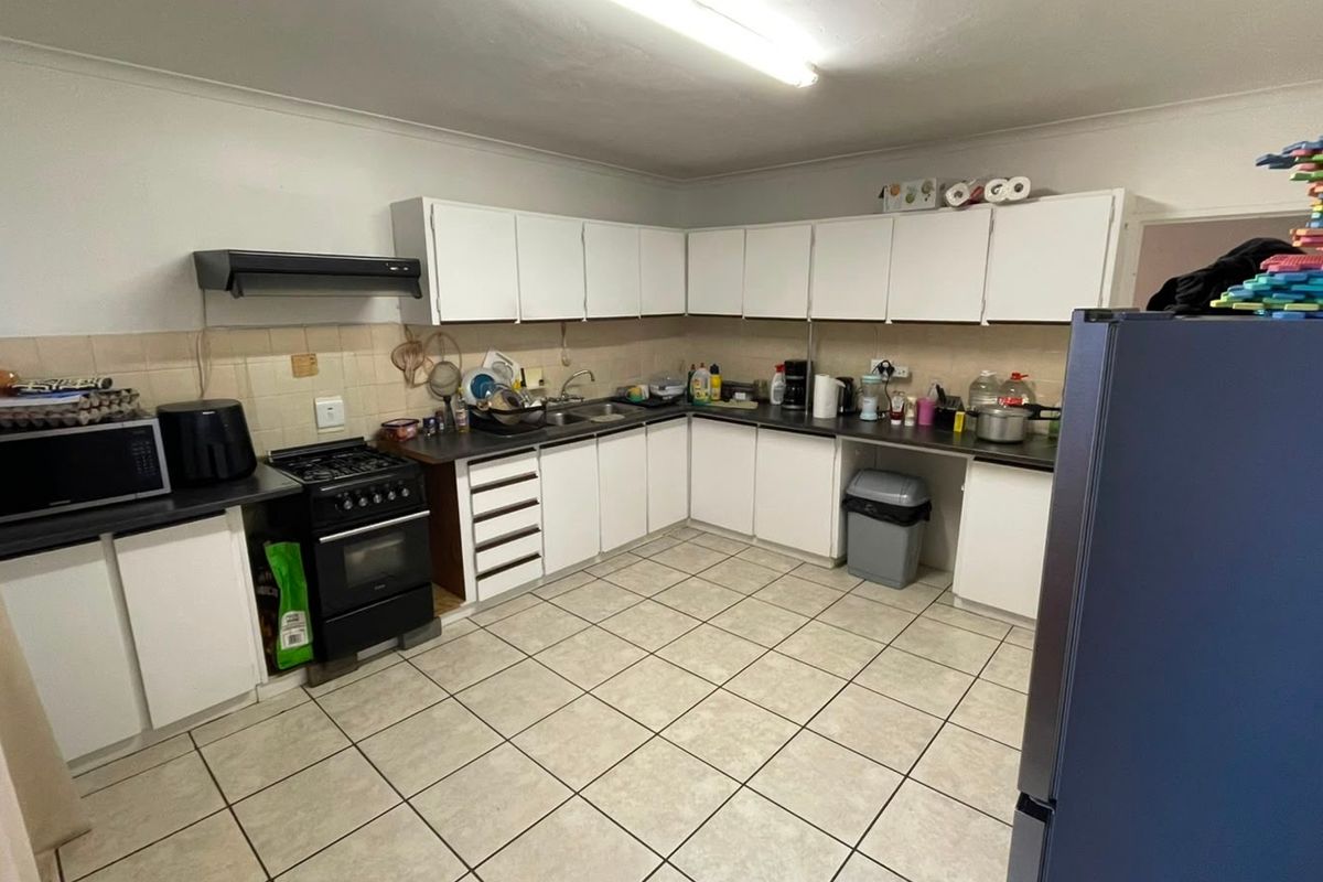 Functional kitchen featuring white built-in cabinetry, laminate countertops, tiled flooring, and a freestanding stove with an extractor fan.