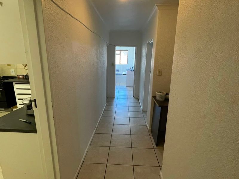 A functional hallway with tiled flooring connecting the kitchen and other living areas, showing signs of wear and requiring cosmetic updates.