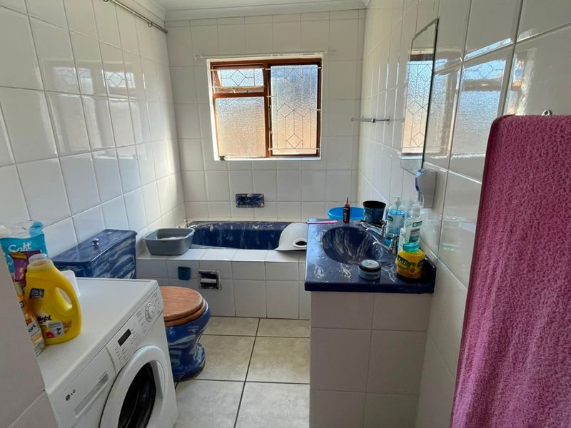 A functional bathroom featuring tiled walls and flooring, a built-in bathtub, and a vanity basin with integrated storage.