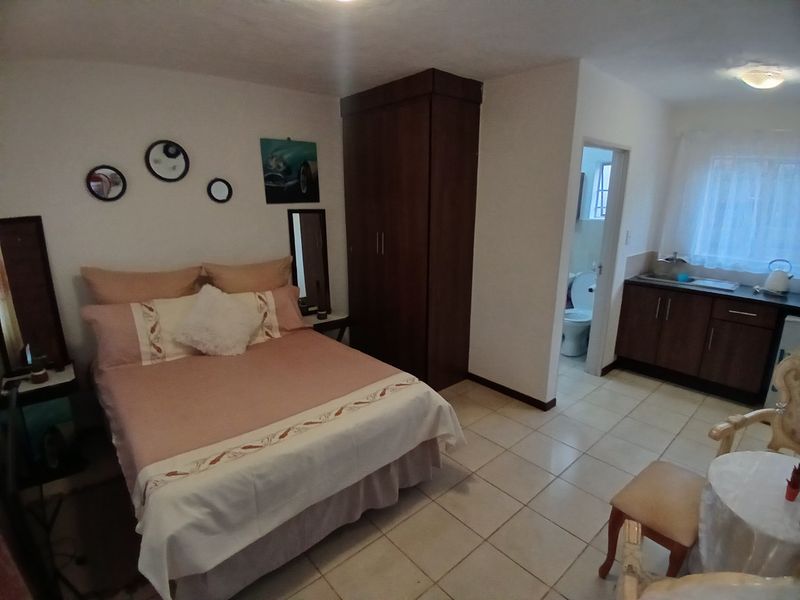 A bedroom featuring tiled flooring, a built-in wardrobe, and an adjoining kitchenette and en-suite bathroom.