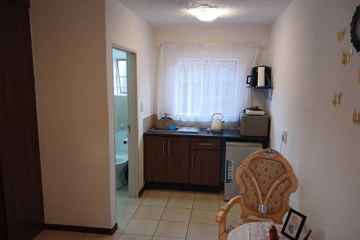 A compact kitchen area featuring dark wood cabinetry, a stainless steel sink, and tiled flooring, with an adjacent bathroom entrance.