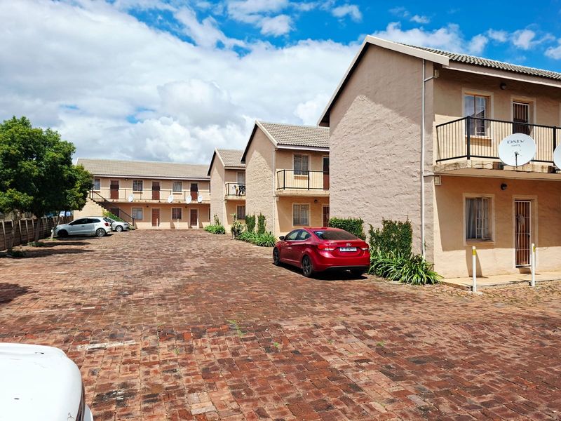 Exterior view of a multi-story apartment complex featuring brick paving, balconies, and dedicated parking areas.