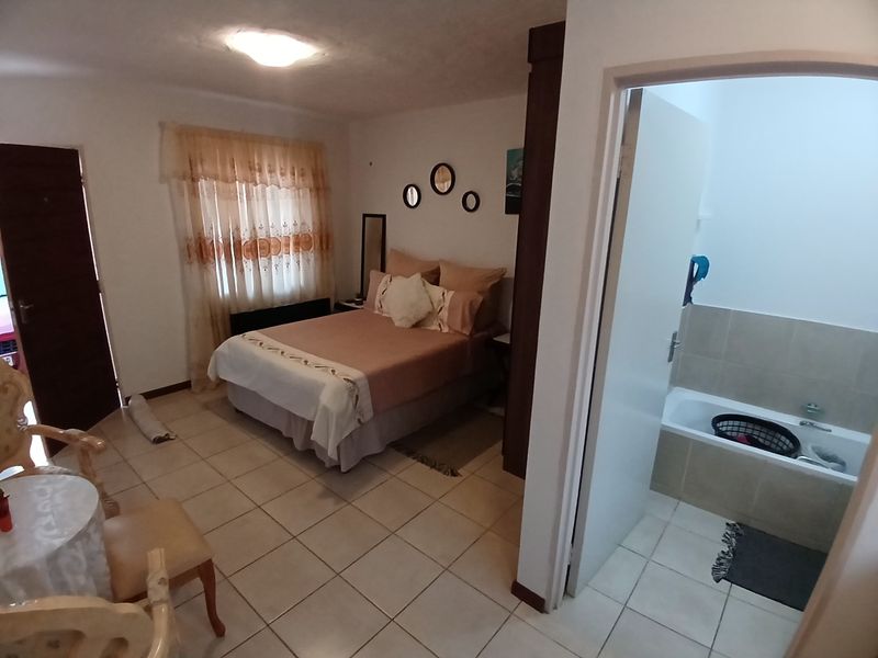 A bedroom featuring tiled flooring and an en-suite bathroom with a built-in bathtub, offering a functional layout with neutral finishes.