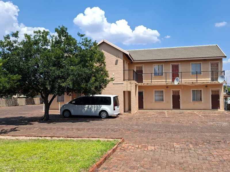 Front exterior view of a two-story apartment building featuring a paved driveway, balcony access, and established landscaping.