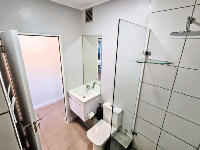 A modern, clean bathroom featuring a wall-mounted vanity, glass shower screen with a rain shower head, and neutral tiled finishes.