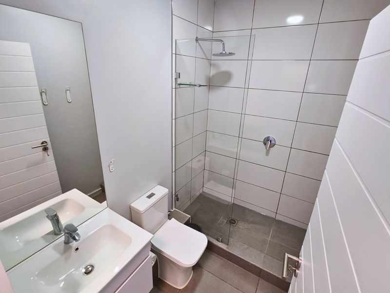 Modern bathroom featuring a walk-in shower with glass screen, vanity basin, and neutral tiling throughout.