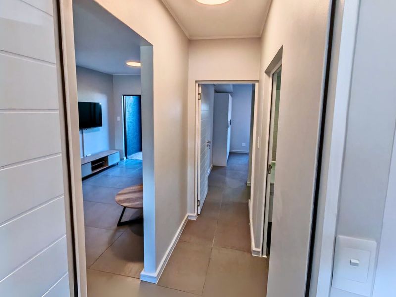 A clean, well-lit hallway featuring neutral wall finishes and tiled flooring, providing access to the living area and adjacent rooms.