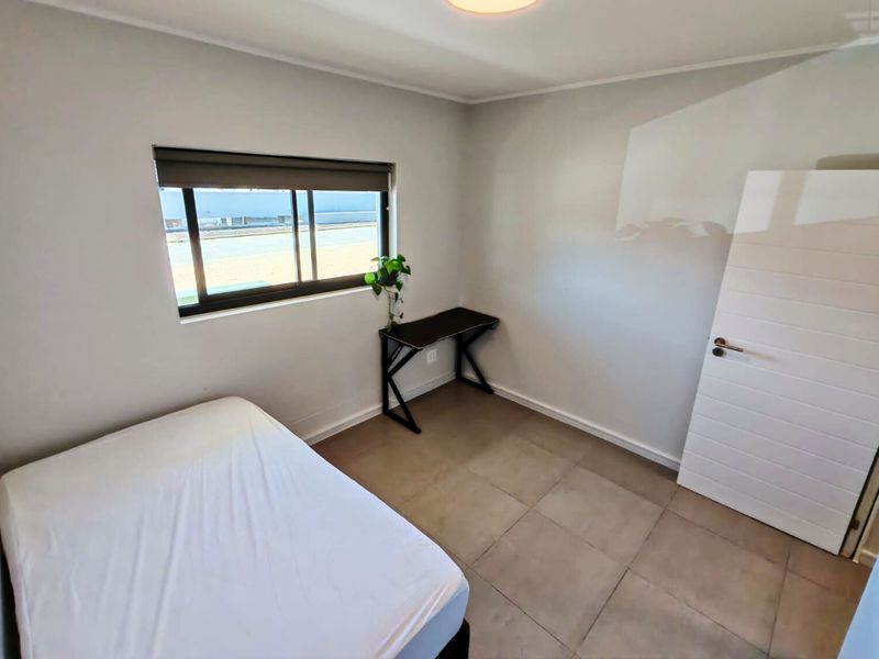 A clean, neutral bedroom featuring tiled flooring, a sliding window with a roller blind, and a modern internal door.