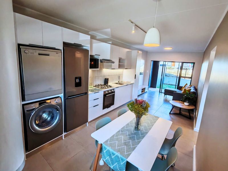 Modern open-plan kitchen and living area featuring sleek white cabinetry, integrated appliances, tiled floors, and direct access to an outdoor patio space.