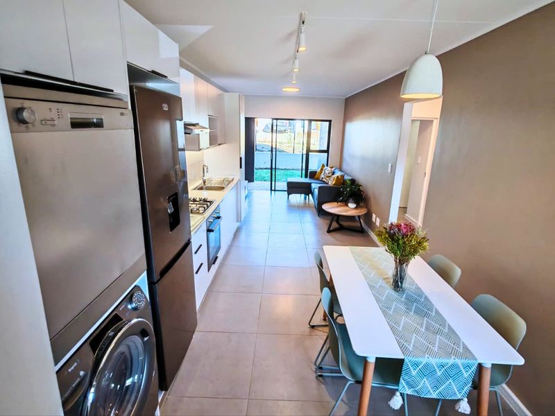 Modern open-plan living area featuring a sleek kitchen with built-in appliances, tiled flooring, and direct access to an outdoor patio through sliding glass doors.