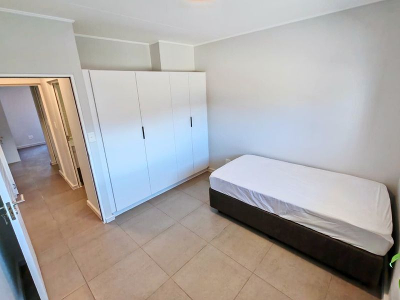 A clean bedroom featuring neutral tiled flooring and ample built-in cupboard storage, offering a functional and well-maintained living space.