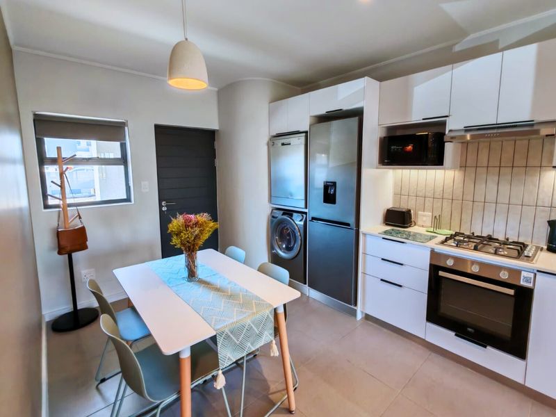 Modern open-plan kitchen and dining area featuring sleek white cabinetry, integrated appliances, gas hob, and tiled flooring.