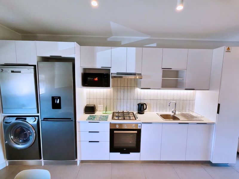 Modern kitchen featuring white cabinetry, gas hob, electric oven, integrated microwave, and stainless steel sink with a clean tiled backsplash.