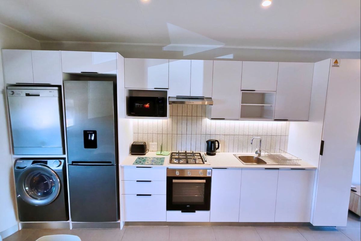 Modern kitchen featuring white cabinetry, gas hob, electric oven, integrated microwave, and stainless steel sink with a clean tiled backsplash.