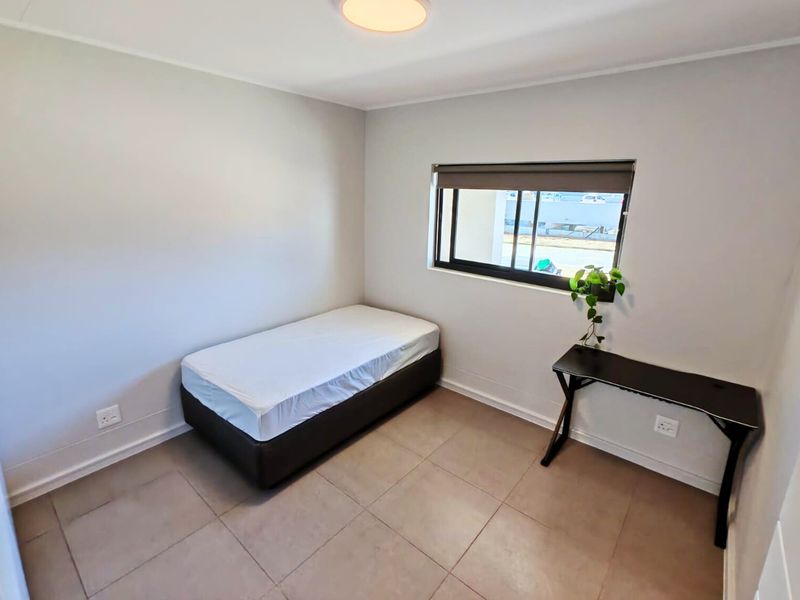 A clean, neutrally painted bedroom featuring tiled flooring, a roller blind, and functional electrical points, offering a simple and well-maintained living space.