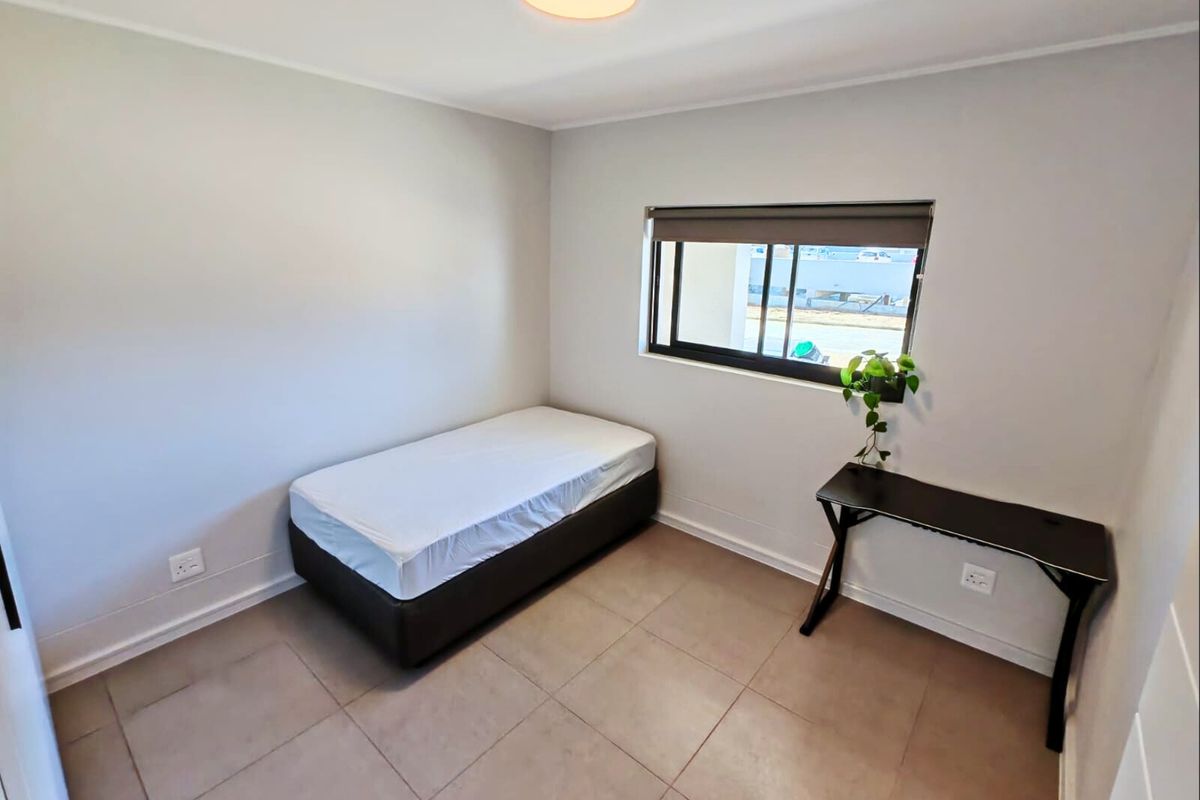 A clean, neutrally painted bedroom featuring tiled flooring, a roller blind, and functional electrical points, offering a simple and well-maintained living space.