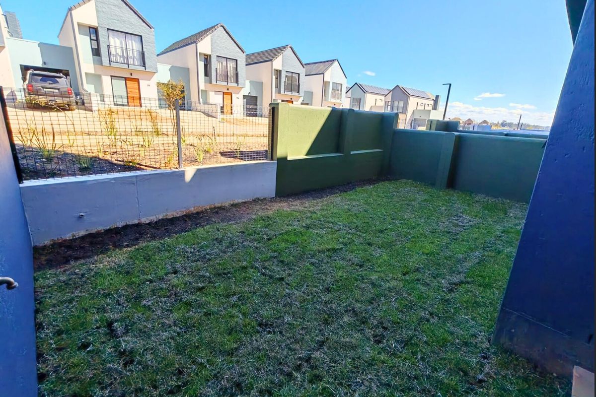 A private rear garden area featuring a lawn, enclosed by a combination of solid boundary walls and wire mesh fencing.