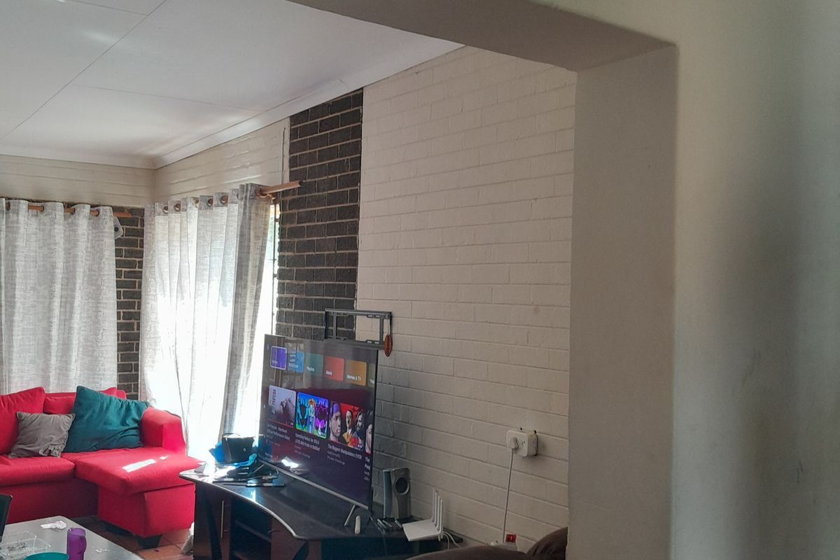 A living room featuring a painted brick accent wall, tiled flooring, and an open-plan layout connecting to adjacent living spaces.