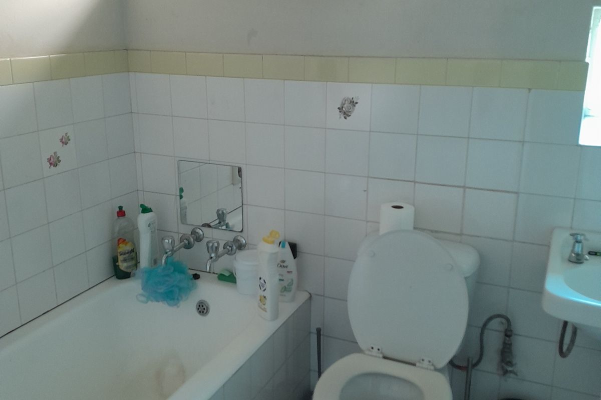A functional bathroom featuring a standard bathtub, toilet, and wall-mounted basin with dated white wall tiling.