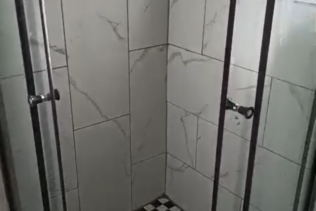 A modern shower stall featuring marble-look wall tiles, a checkered floor pattern, and a glass enclosure with security bars on the window.