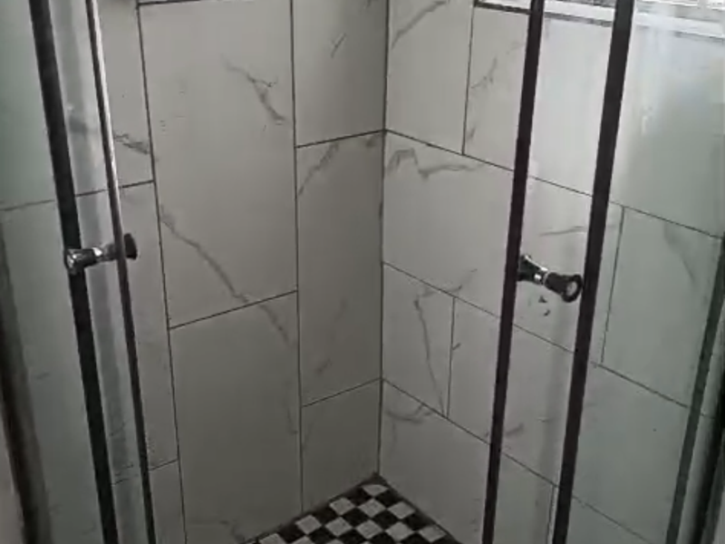 A modern shower stall featuring marble-look wall tiles, a checkered floor pattern, and a glass enclosure with security bars on the window.