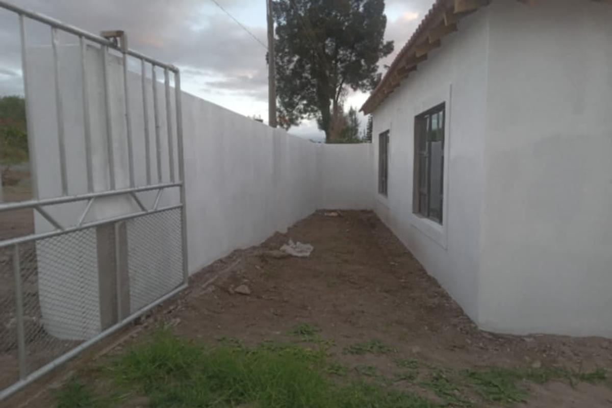 Exterior view of the property showing a perimeter wall, metal gate, and unfinished ground area surrounding the building structure.