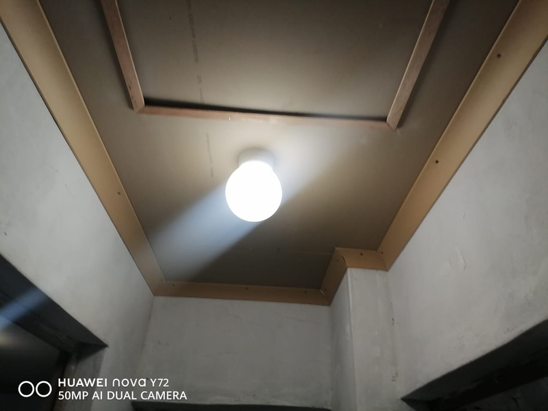 A view of an unfinished ceiling area featuring a central light fixture, exposed plasterboard, and wooden trim detailing.