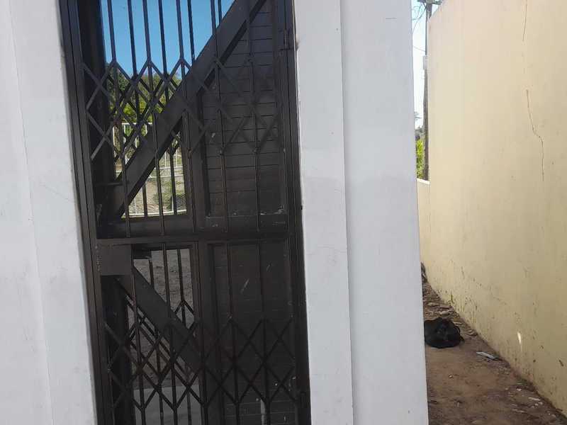 Exterior view of a rear access point featuring a metal security gate and a boundary wall showing signs of wear and cracking.