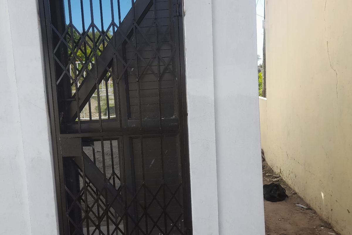 Exterior view of a rear access point featuring a metal security gate and a boundary wall showing signs of wear and cracking.