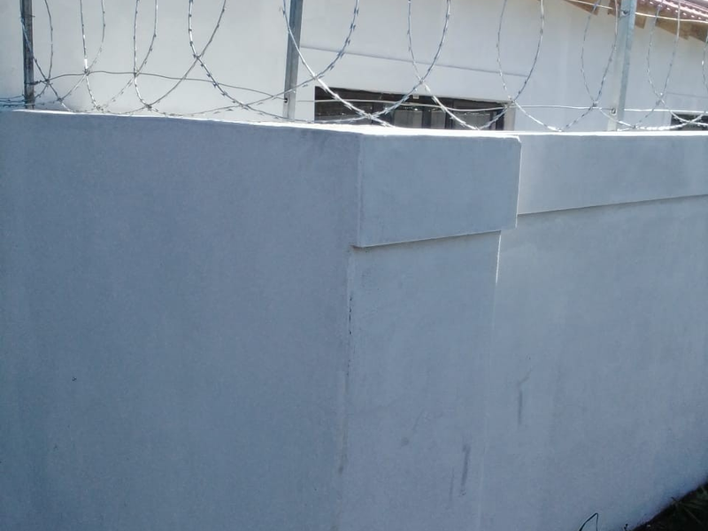 Exterior view of a perimeter wall featuring security razor wire and a tiled roof section.
