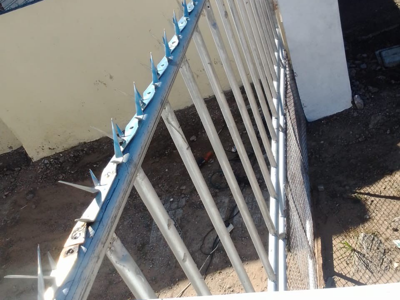Exterior view of the property boundary featuring metal security fencing with spiked topping and a masonry wall.