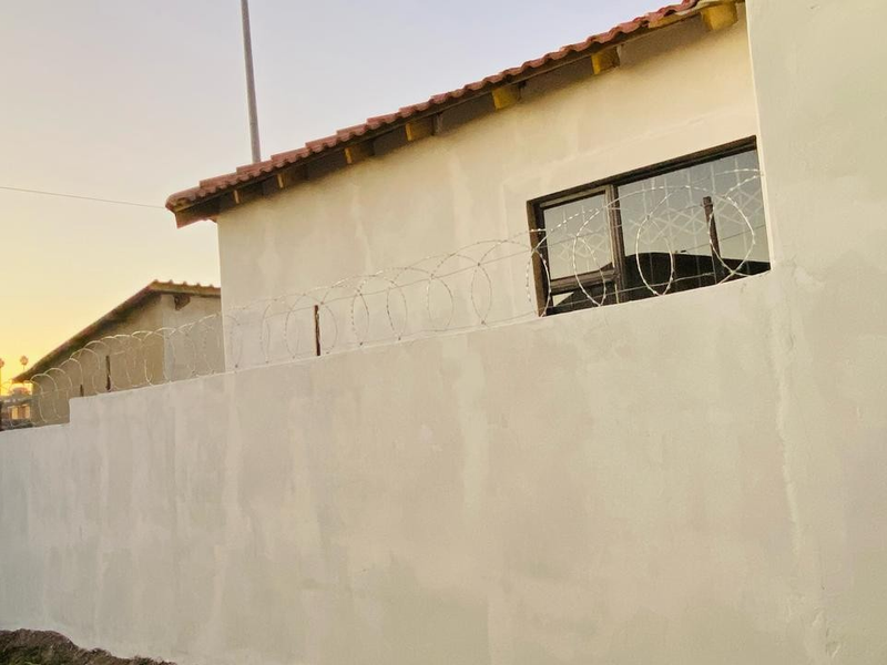 Exterior view of the property showing a perimeter wall with razor wire and a tiled roof section.