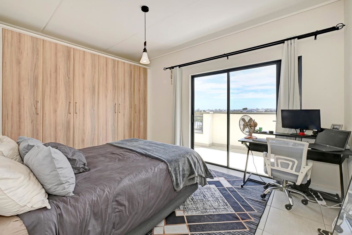 A well-lit bedroom featuring extensive built-in cupboards, tiled flooring, and a sliding glass door providing access to a private balcony with city views.