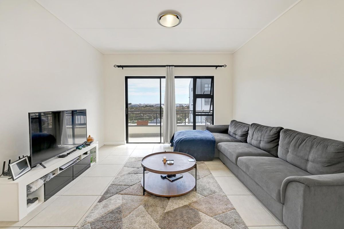 A bright living room featuring tiled flooring and a large sliding glass door that opens onto a balcony with scenic views.