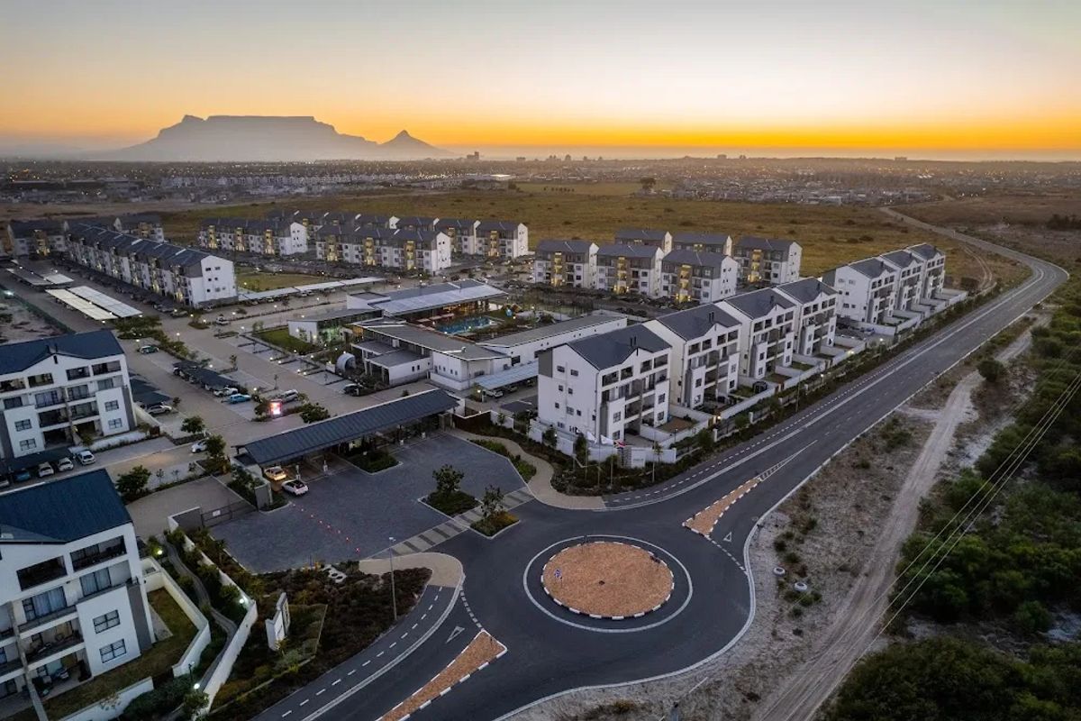 Aerial view of a modern residential apartment complex featuring landscaped grounds, communal facilities, and secure gated access with Table Mountain in the background.