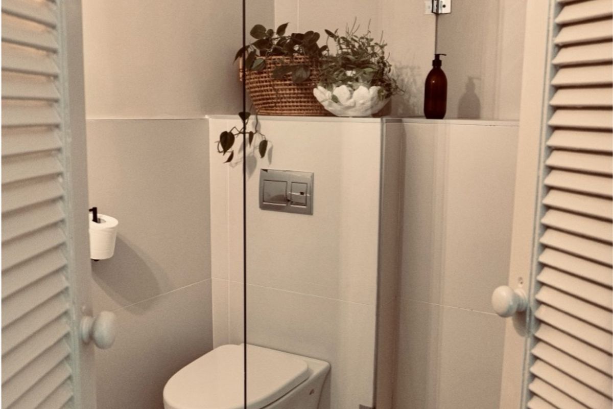 A compact, modern bathroom featuring a wall-mounted toilet, glass shower partition, and neutral tiled finishes.