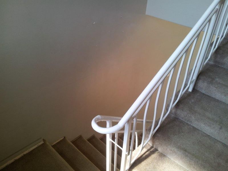 A staircase with a white metal balustrade and carpeted steps, showing signs of wear on the walls and flooring.