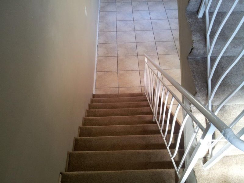 A view looking down a carpeted staircase with a metal balustrade, leading to a tiled lower level hallway.