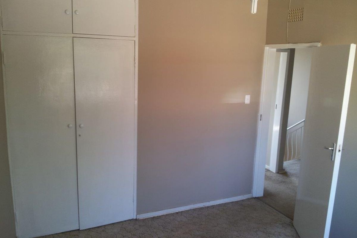 An empty bedroom featuring built-in cupboards, carpeted flooring, and neutral wall tones, offering a blank canvas for potential updates.